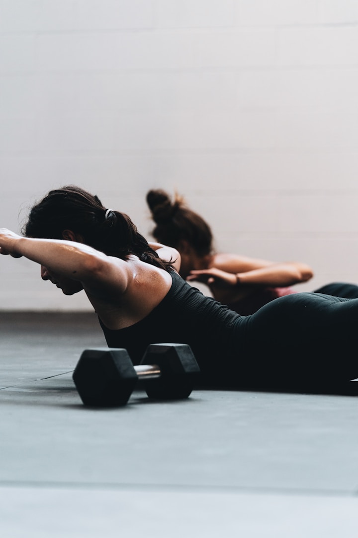 Zwei Personen führen Liegestütze mit Hanteln auf einer Fitnessmatte aus.